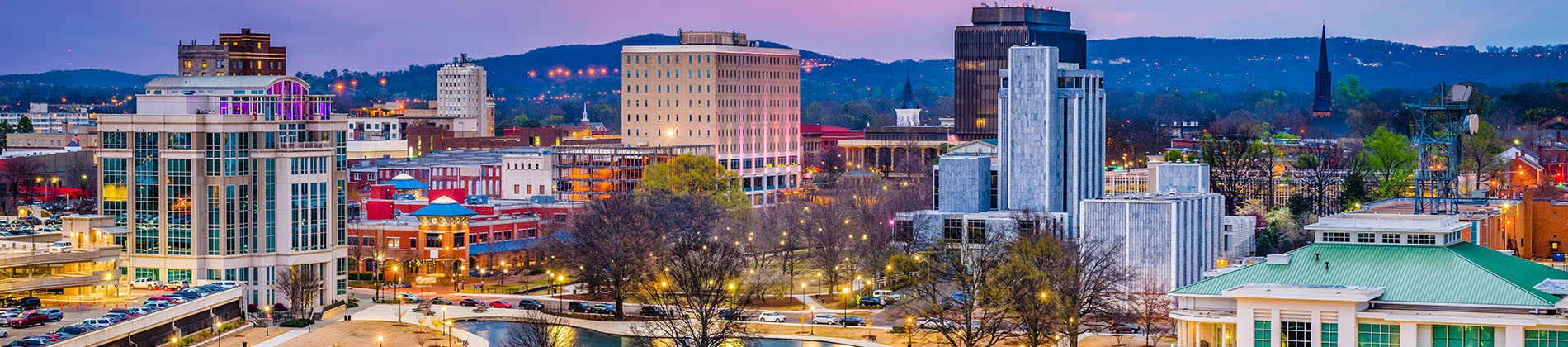 The image shows a cityscape at dusk with a prominent skyline featuring buildings and a bridge, set against a gradient sky transitioning from warm to cool colors, suggesting an urban environment during evening hours.