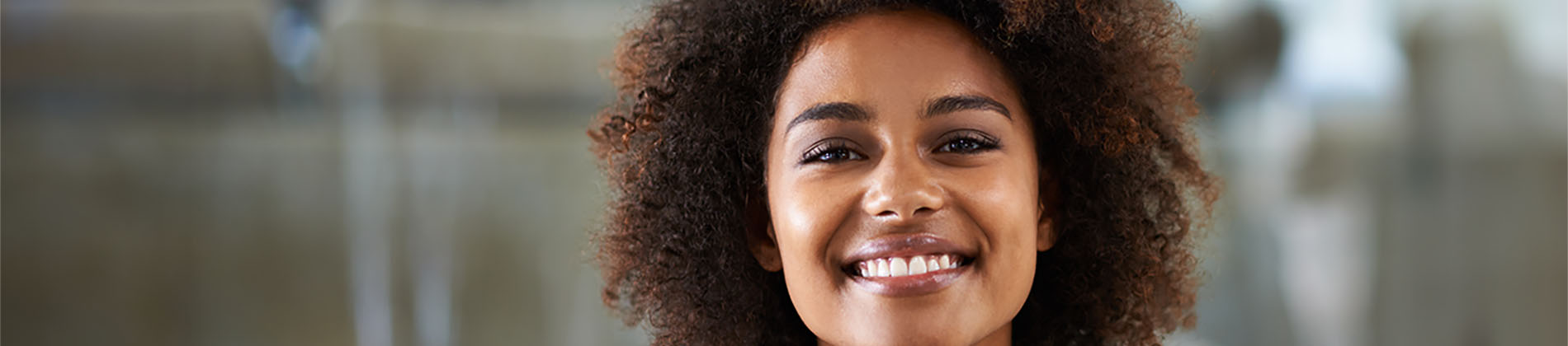 The image is a photograph of a woman with light skin, smiling at the camera. She appears to be in her late twenties or early thirties and has long hair. Her eyes are looking directly at the camera, and she is holding up her index finger near her mouth as if she s making a point or emphasizing something. The background is plain and light-colored, which suggests that this could be a stock photo used for various purposes such as advertising, personal branding, or lifestyle content.