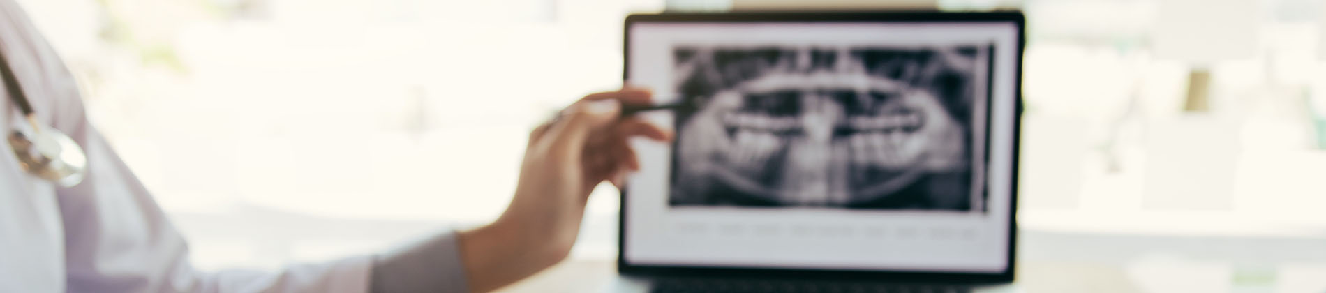 A person is seated in a dental chair, receiving care from a dental professional who stands behind them.