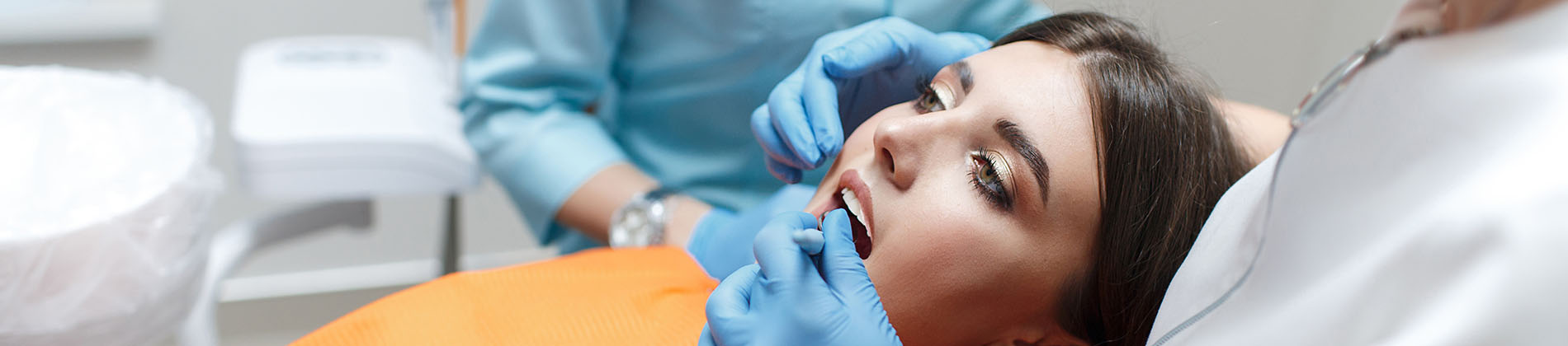 A woman lying in bed with her eyes closed while a medical professional attends to her, wearing a surgical mask and gloves.