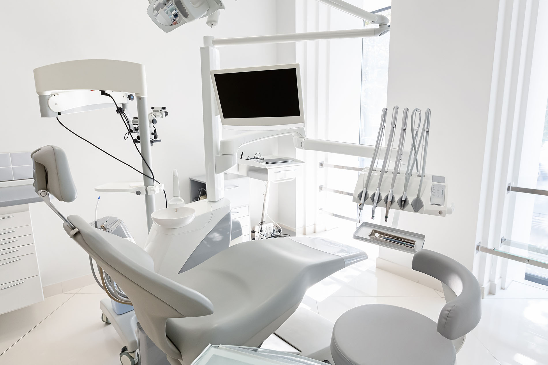The image shows a modern dental office interior with a dental chair, examination equipment, and a computer monitor displaying a patient s X-ray.