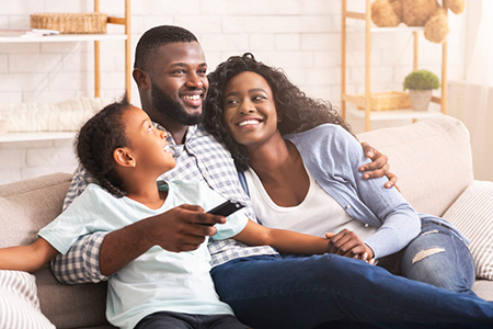 A family of four sitting on a couch with smiles on their faces, watching television together.