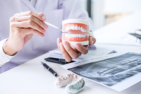 The image shows two photographs side by side  on the left, a person wearing a white lab coat holds an open mouth model, examining it closely  on the right, the same individual is seen holding a toothbrush and dental floss while standing in front of a desk with various dental-related items.