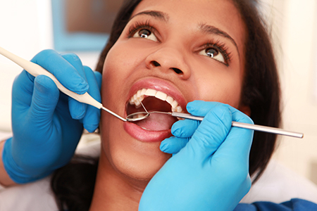 The image depicts a person receiving dental care from a professional, with a focus on a close-up of their mouth and teeth being worked on by another individual wearing gloves and using tools associated with dental procedures.