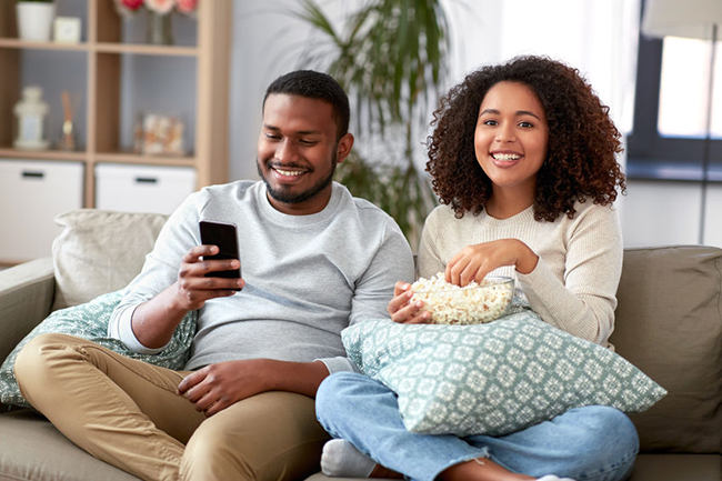 A man and woman are sitting on a couch, enjoying a movie together with popcorn.