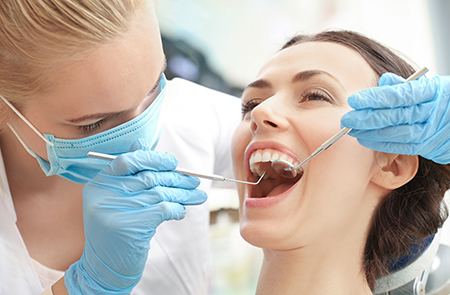 A dentist performing dental work on a patient s teeth while wearing protective gloves and a mask.